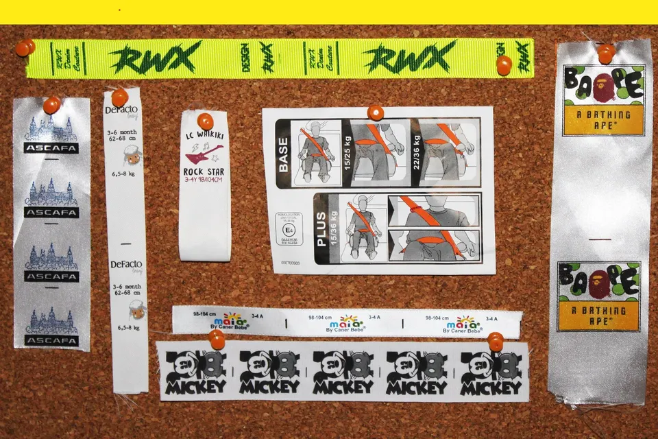 White satin care labels pinned to a cork board with neon yellow printed brand tapes